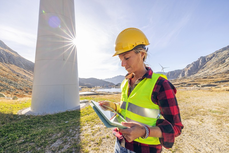 Energy and utilities worker looks at tablet while maintaining a wind power plant