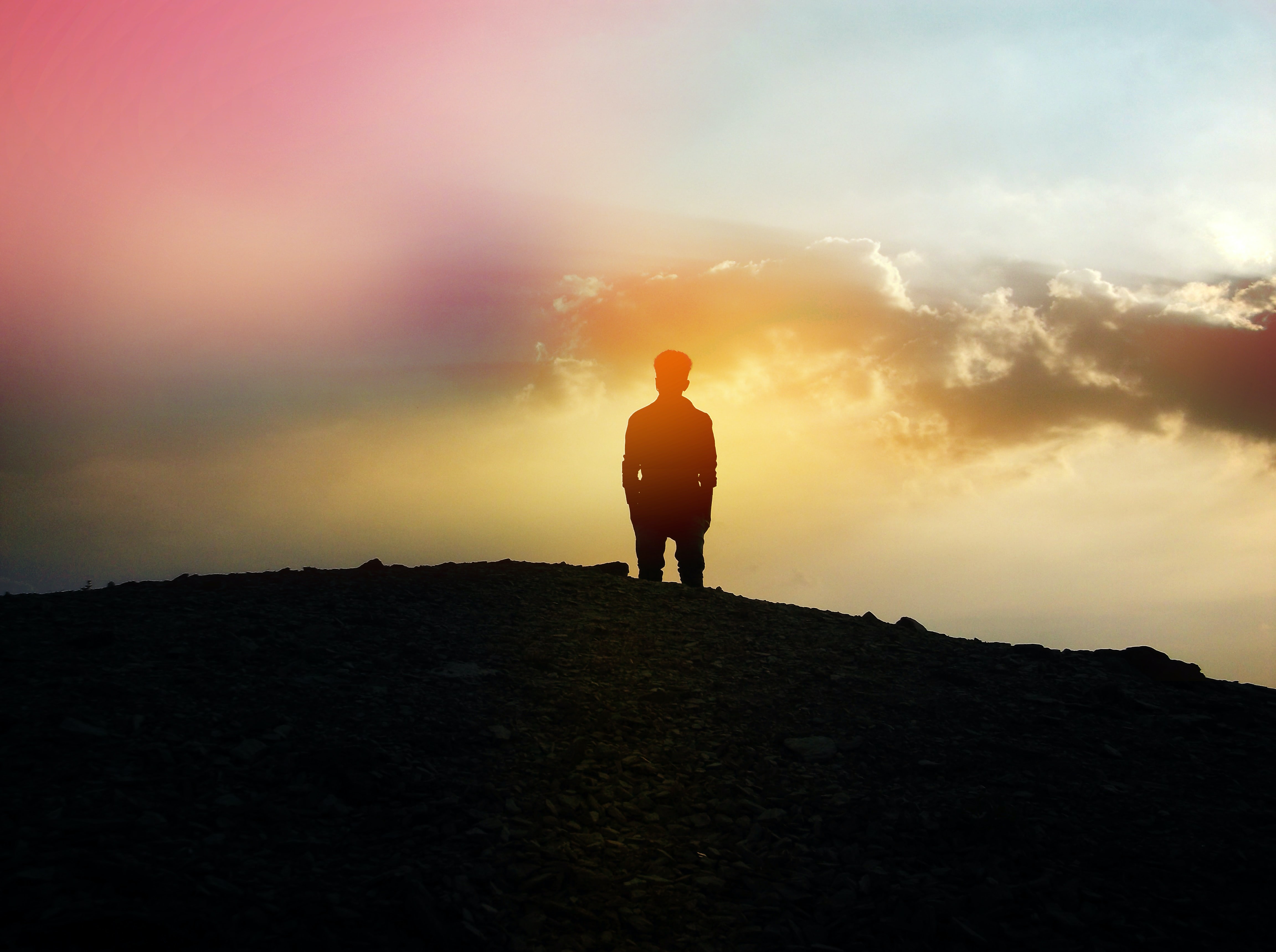 Man stands on hill and looks at the sun rise in the horizon