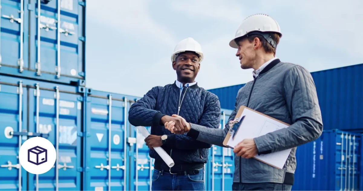 Ein Logistikdepot mit LKWs. Zwei Männer schütteln sich im Vordergrund die Hand