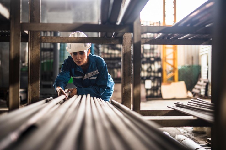 Een arbeider stapelt ijzeren buizen op een plank in een fabriek 