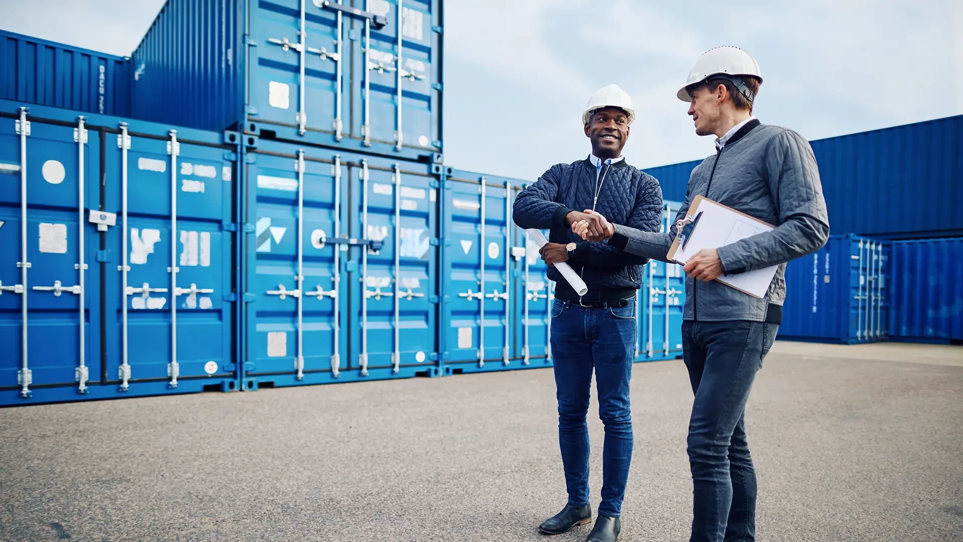 Due uomini in un deposito di container si stringono la mano