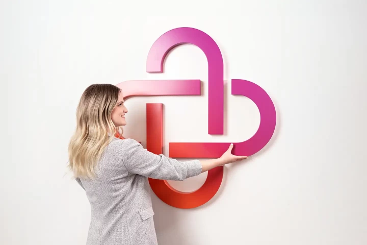 Eine Unite Mitarbeiterin hält das Firmen-Logo an die Wand und lächelt. 