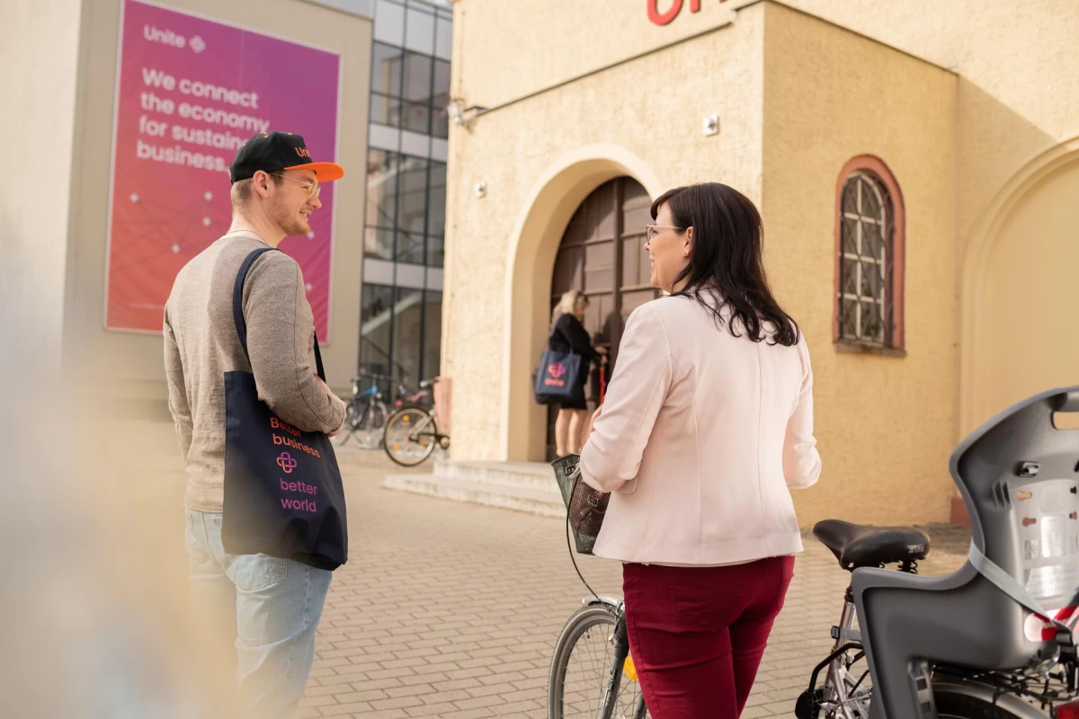 Zwei Menschen stehen vor einem Gebäude, eine Frau hinten schließt eine Tür auf