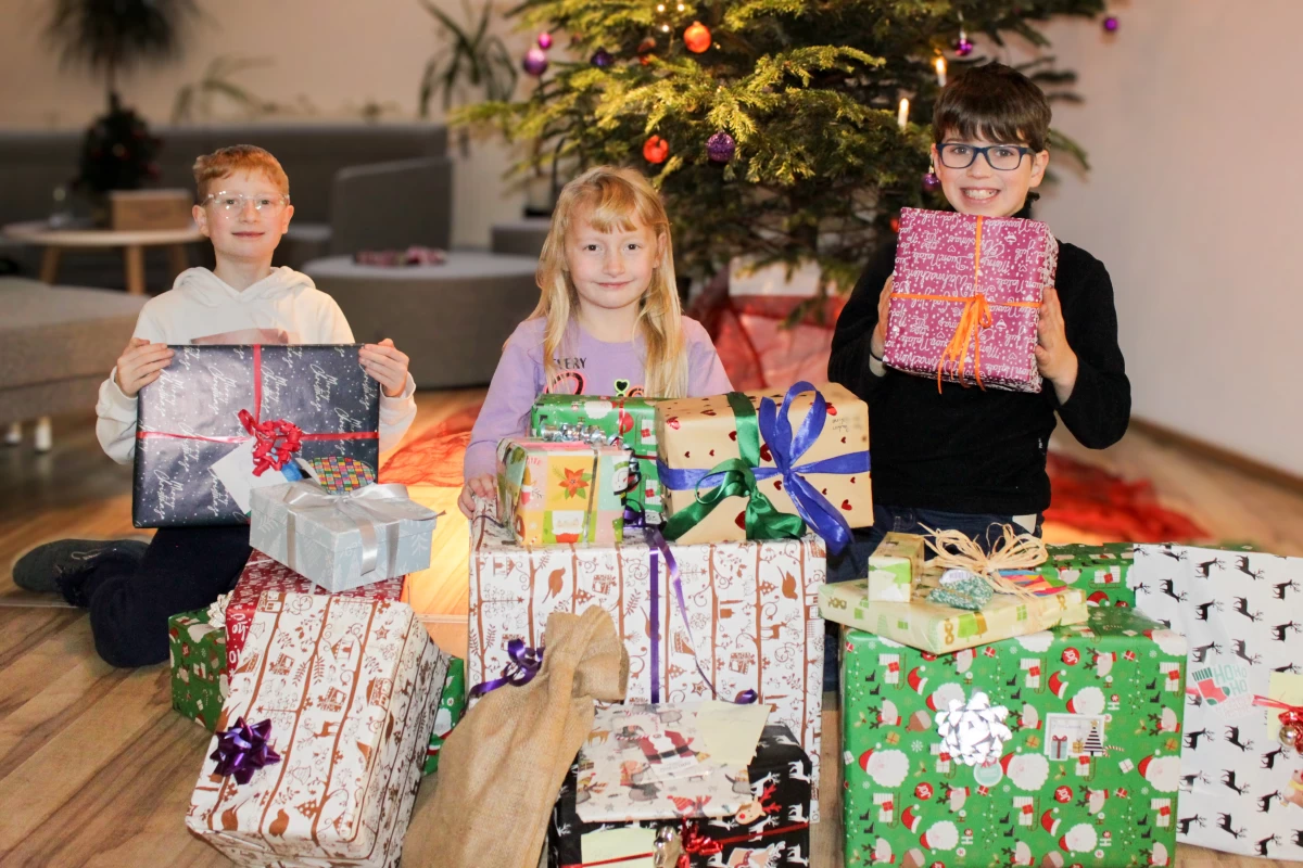 Kinder halten Geschenke in den Händen, im Hintergrund ist ein Weihnachtsbaum