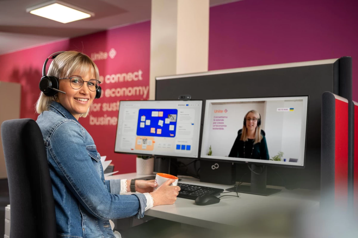 Eine Frau sitzt in einem Büro vor einem Bildschirm und dreht sich zur Kamera um