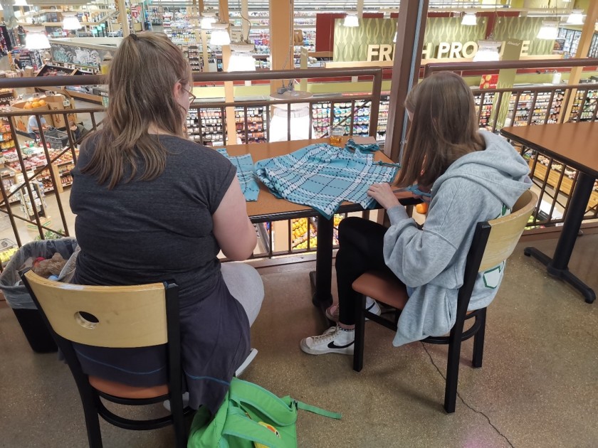 Zwei junge Menschen sitzen an einem Tisch und stellen Kuscheldecken für ein Tierheim her