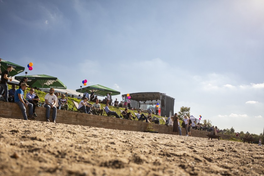 Menschen auf dem Unite Sommerfest sitzen in Sonnenstühlen am Strand. Im Hintergrund steht eine Bühne