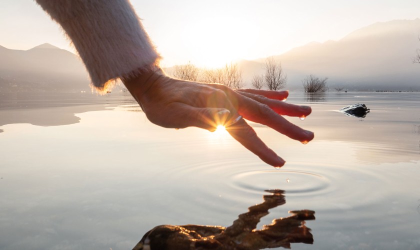 Een hand raakt een oppervlak bedekt met water aan en de zon reflecteert op het water