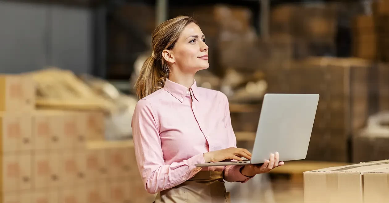 Vrouw met laptop in hand in een magazijn met dozen