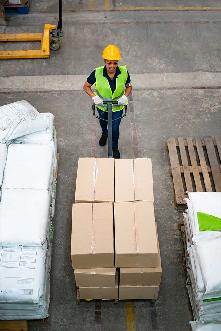 Une employée logistique manipulant un tire palette chargé de cartons