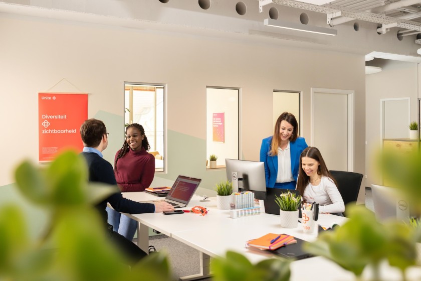 Das Foto zeigt in einem Büro vier verschiedene Menschen, die miteinander sprechen und arbeiten.