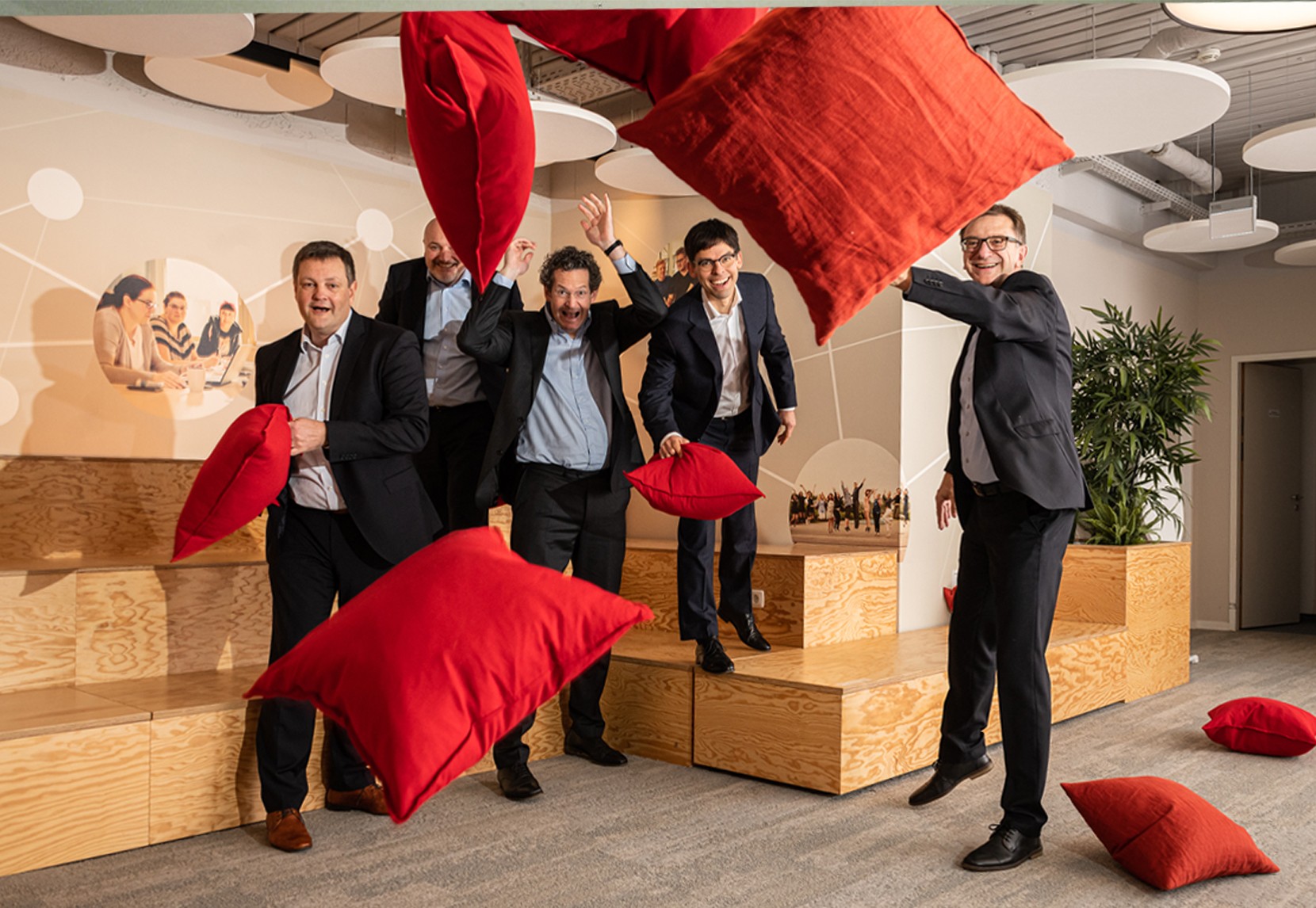 Five men in suits throwing pillows at the camera