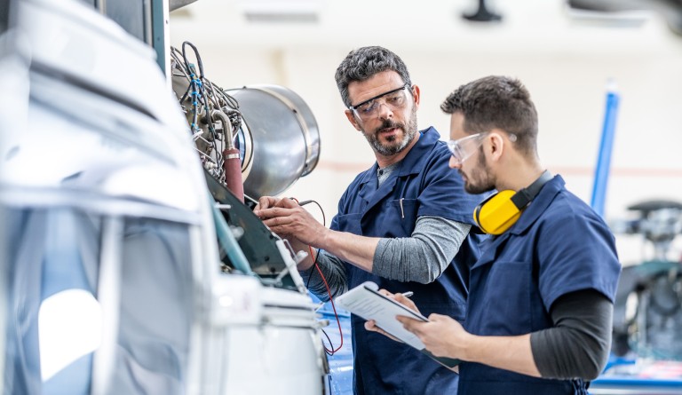 Zwei Männer in Arbeitsschutzkleidung, die eine Maschine warten.